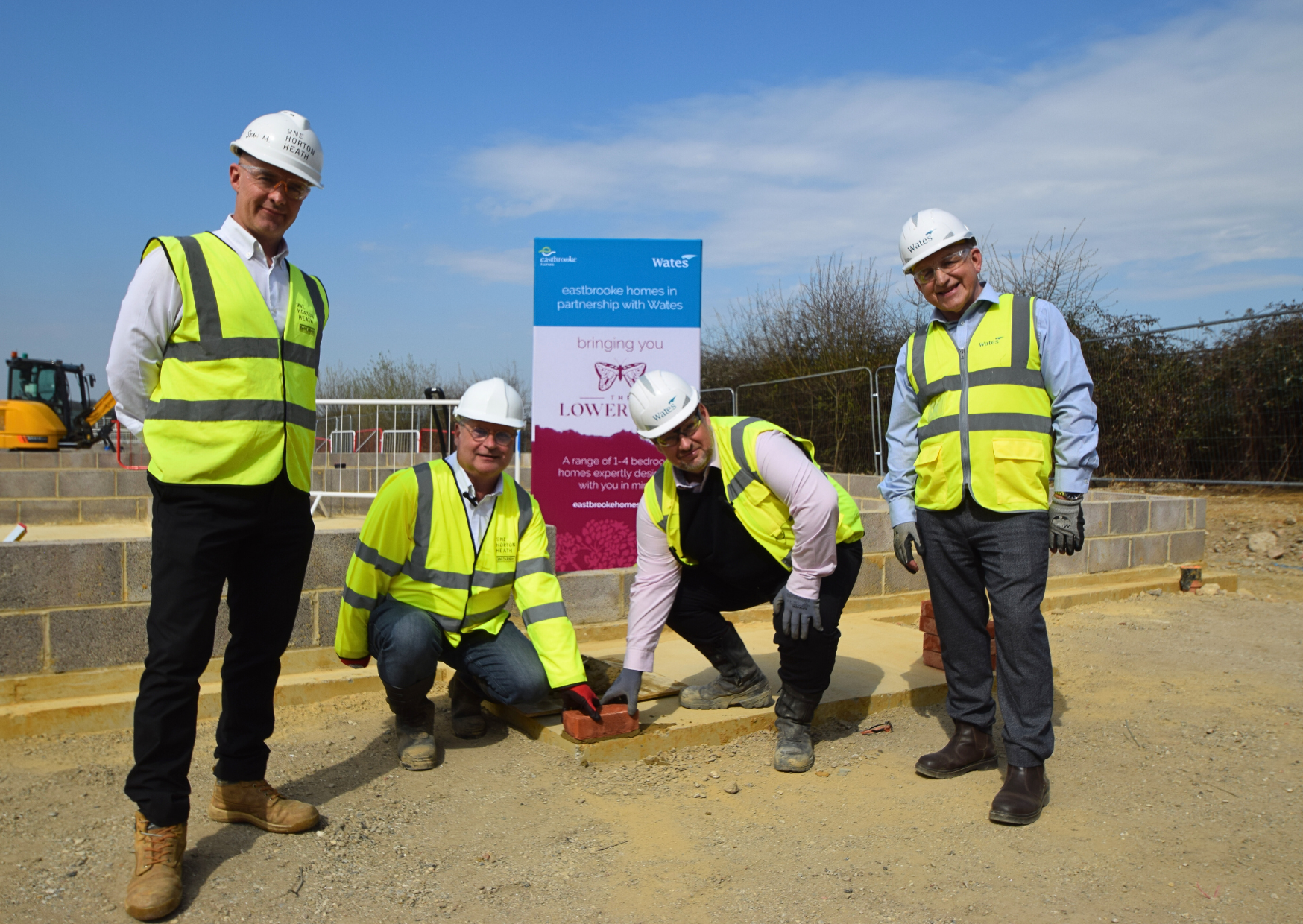 4 men in high-vis and hard hats laying e foundation stone