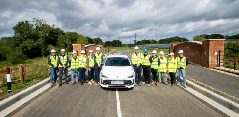 white car in the middle of a new road with construction staff wearing hi-vis white car in the middle of a new road with construction staff wearing hi-vis