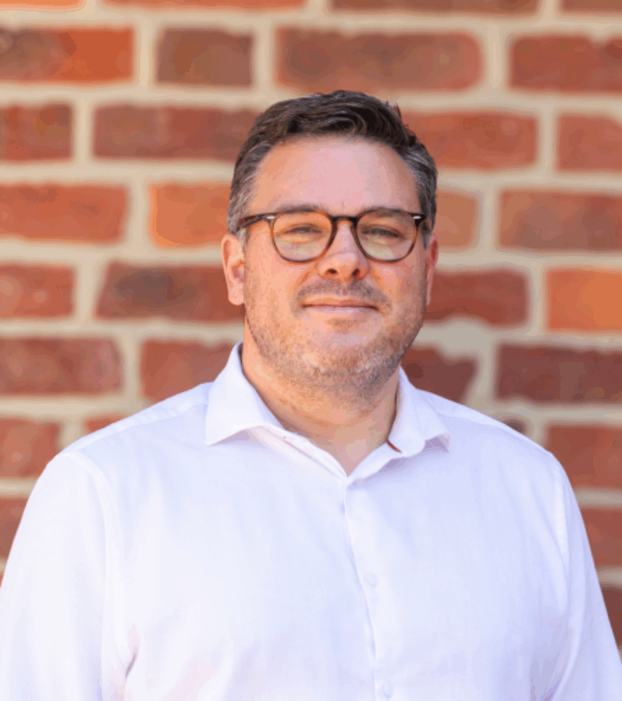 Shot of a man smiling with round glasses, dark hair and a white shirt