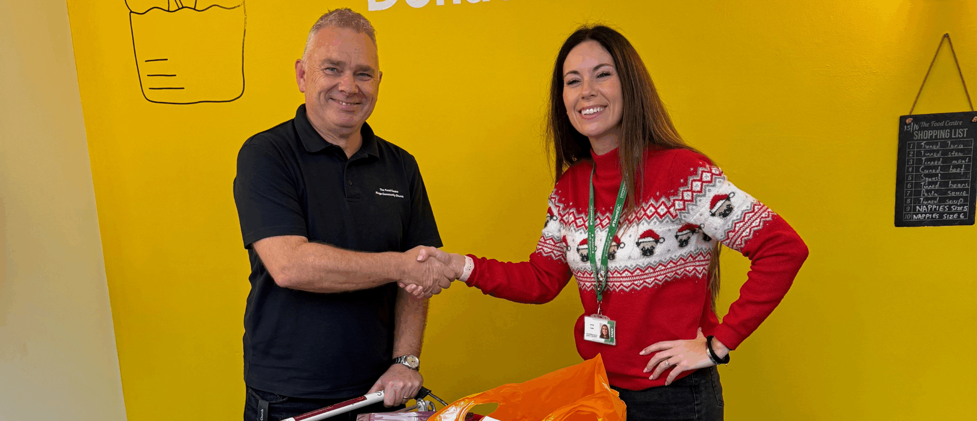 Landscape Image - a man and a lady shaking hands with a donated trolly of food donations