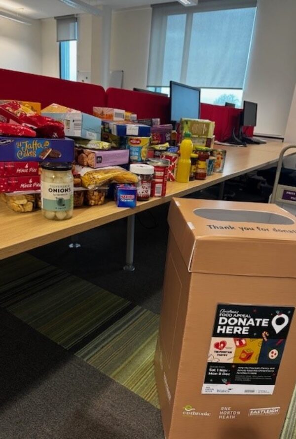 A desk of donated food with a collection bin for a festive food drive