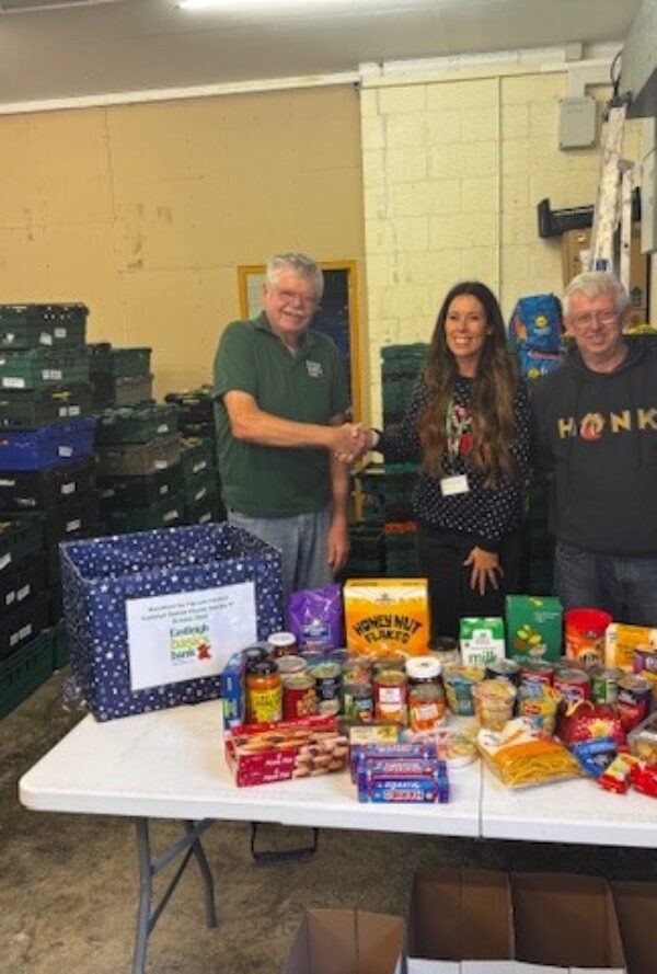 2 man and a woman shaking hands at a food warehouse with donated goods on a table