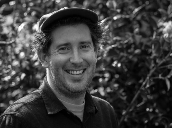 man with hat smiling and a leafy background (in black and white)