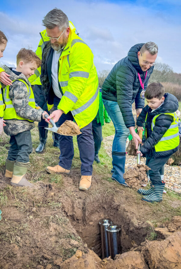 Adults and school children in high-vis shoveling dirt to bury a time capsule