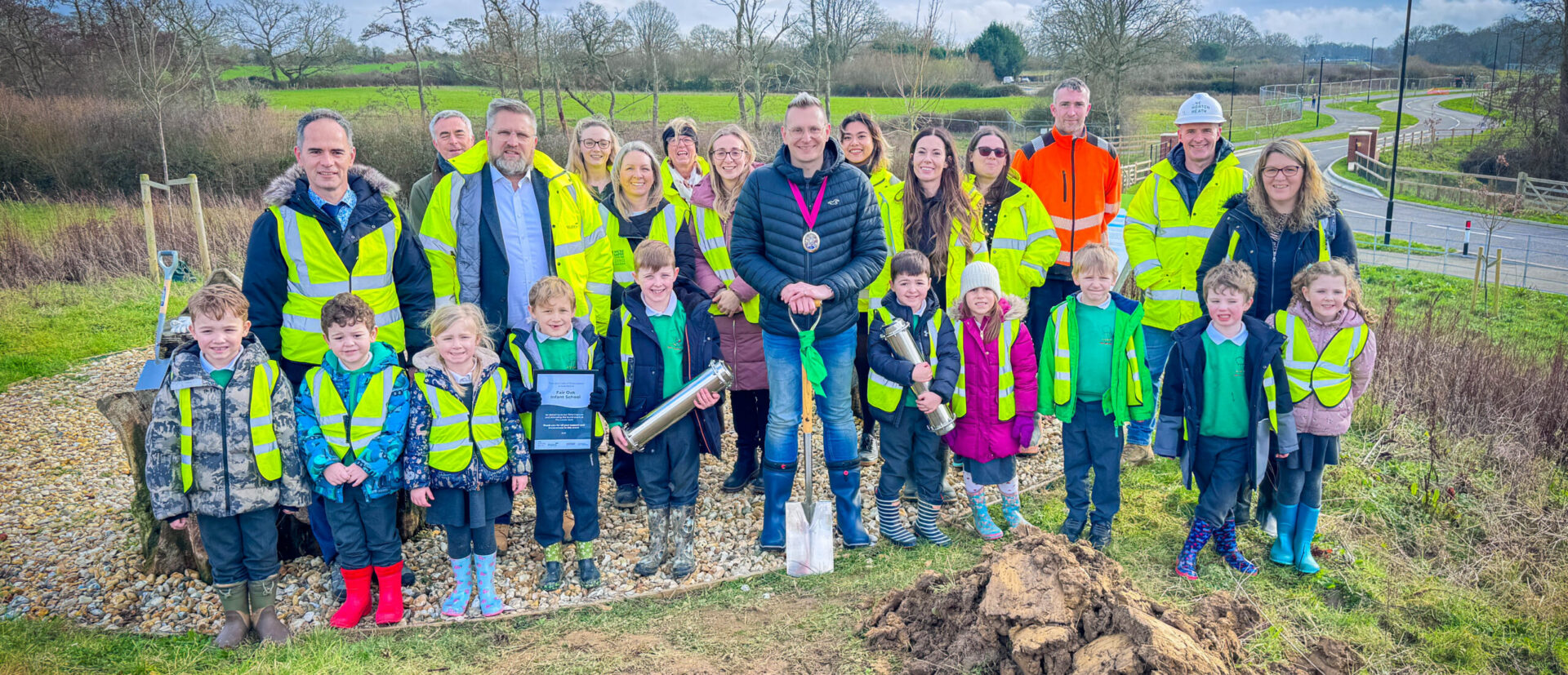 School children an adults dressed in high-vis burying a time capsule in a whole in the ground
