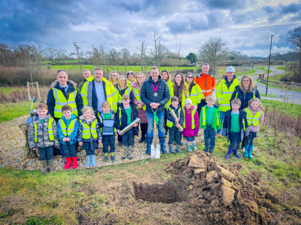 School children an adults dressed in high-vis burying a time capsule in a whole in the ground