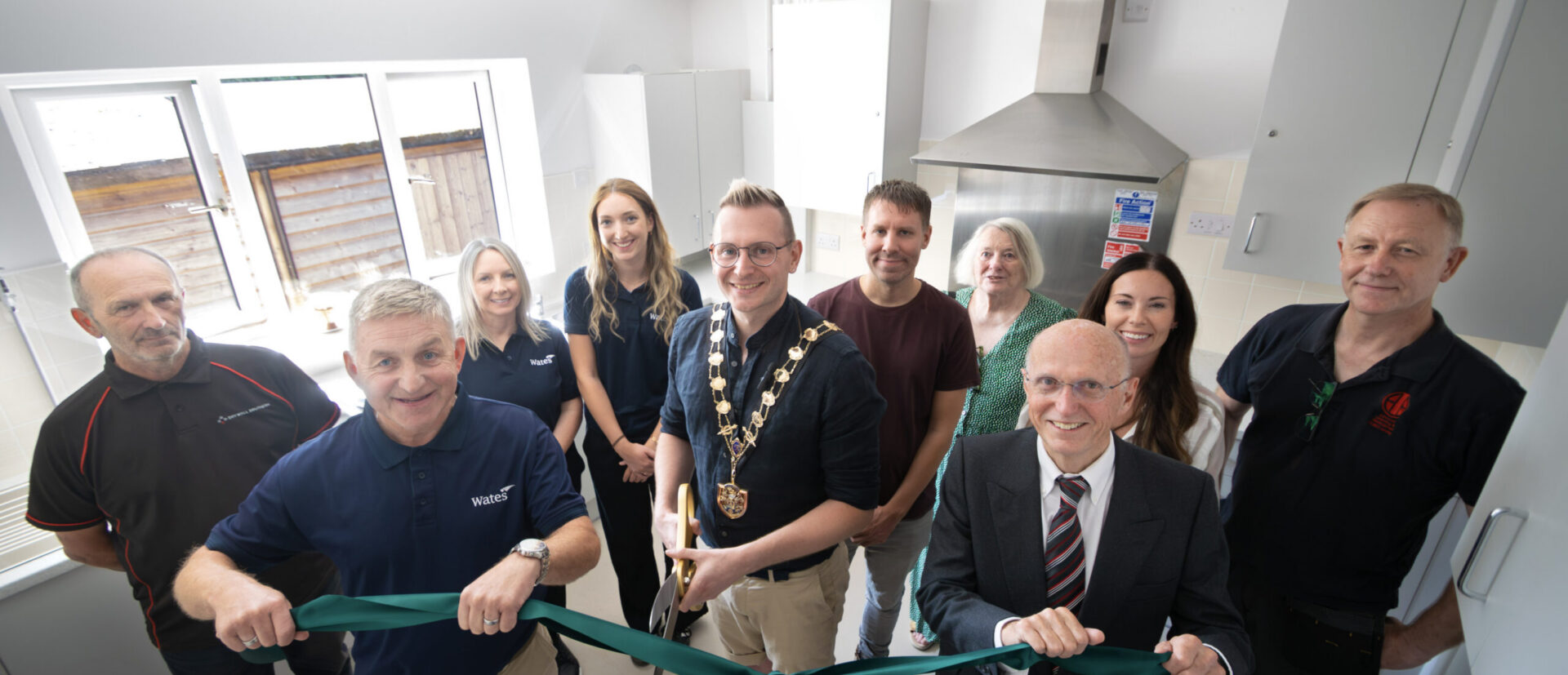 A group of people in a new village hall kitchen - ribbon cutting event with the Mayor cutting a green ribbon