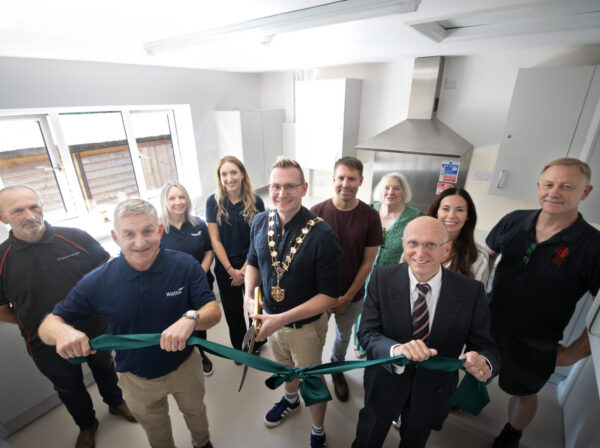 A group of people in a new village hall kitchen - ribbon cutting event with the Mayor cutting a green ribbon