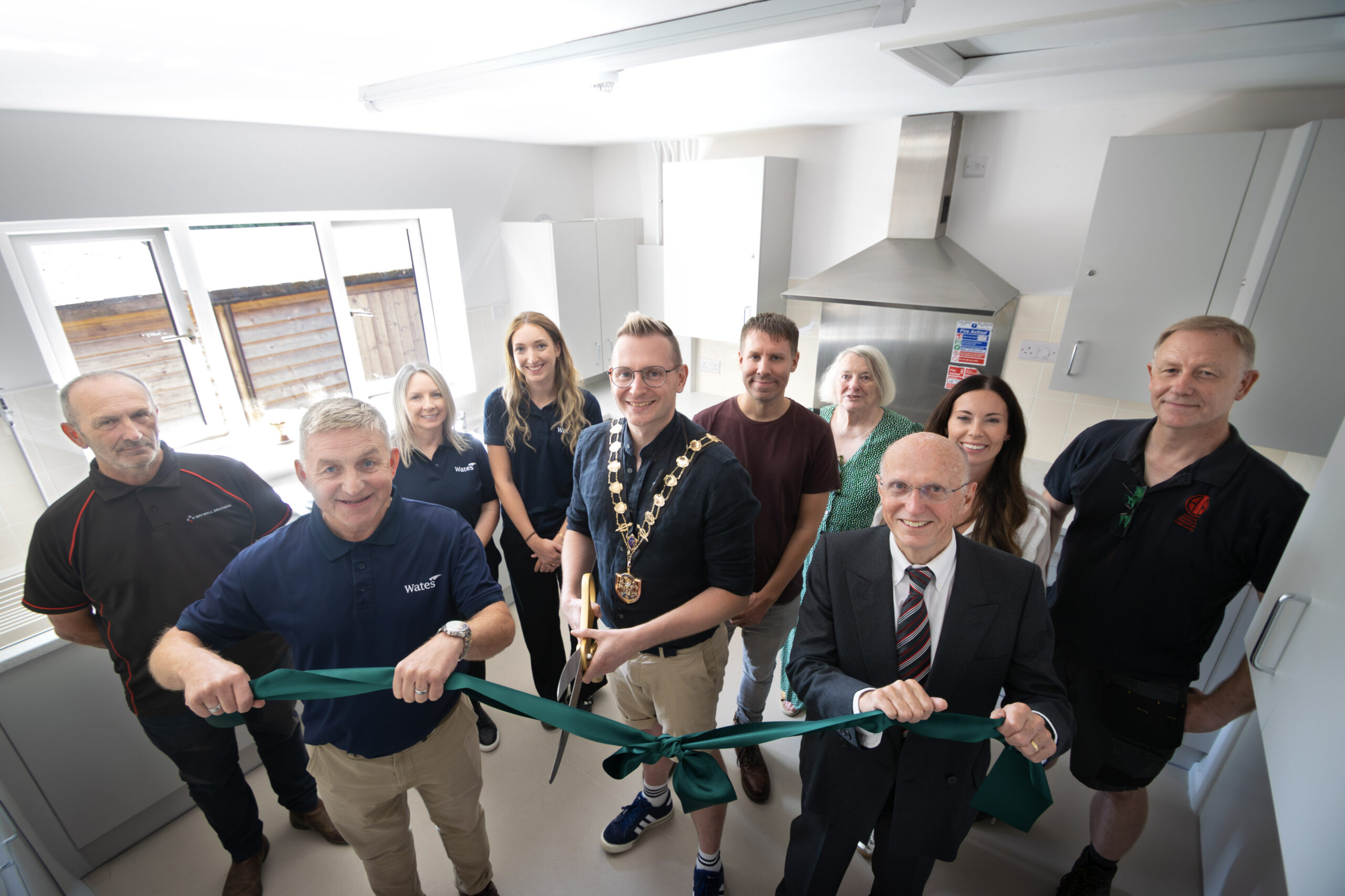 A group of people in a new village hall kitchen - ribbon cutting event with the Mayor cutting a green ribbon