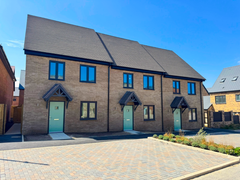 3 homes - attached - with green doors, and 3 windows each - new build homes at The Lower Acre Development.