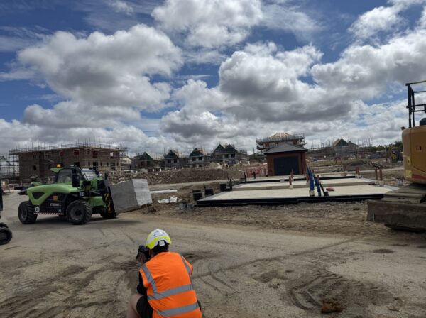 Person kneeling down to take a picture dressed in high-vis. Photographing a green electric telehandler.