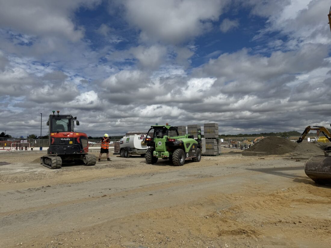 Person in-between 2 construction vehicles taking a picture and dressed in high-vis.