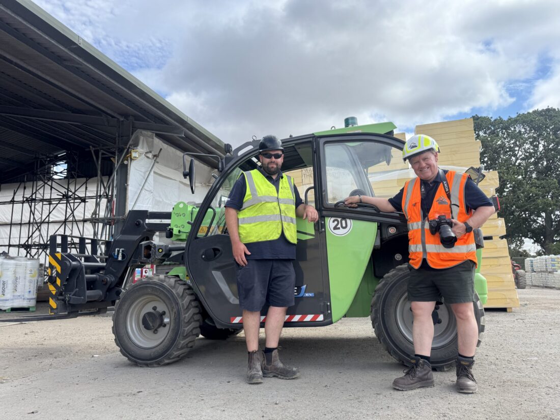 2 mean dressed in hi-vis leaning on an electric green telehandler vehicle.
