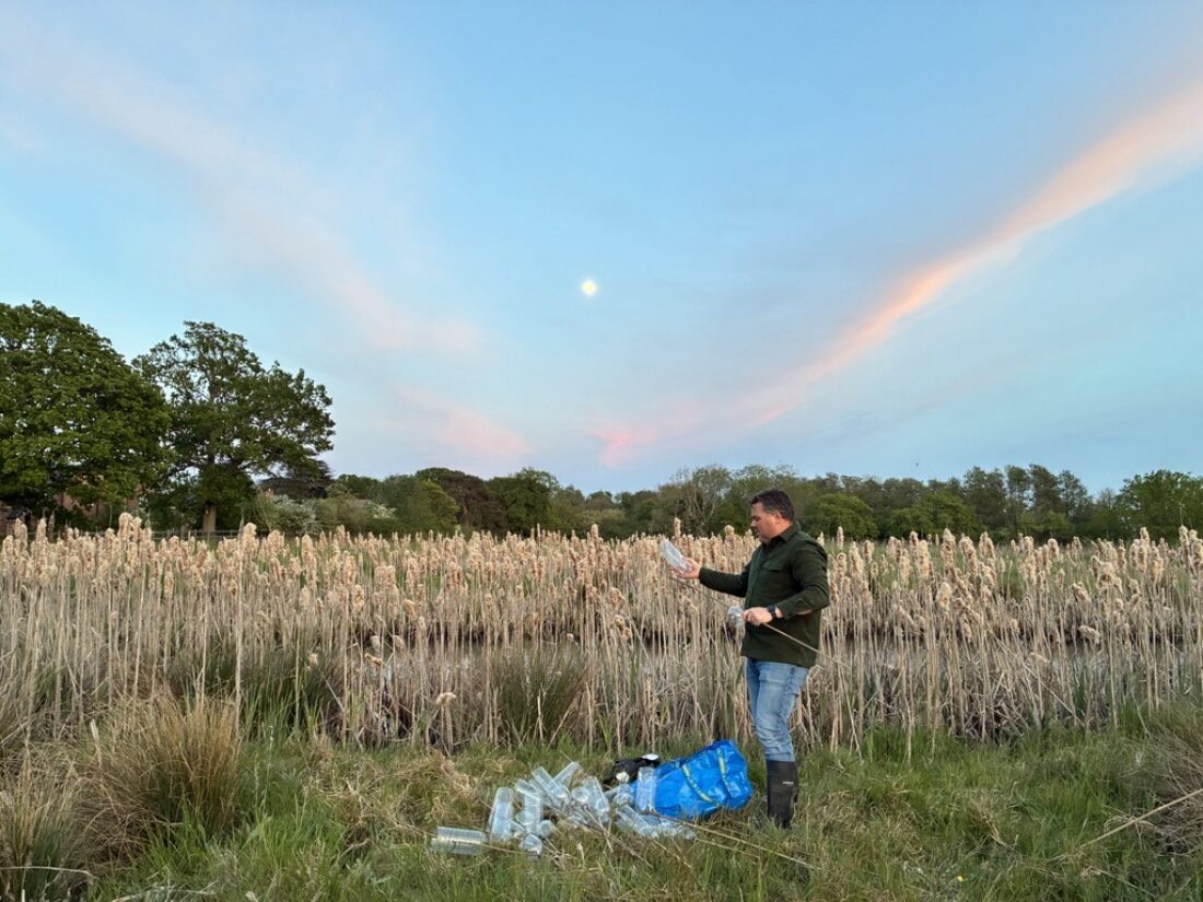 Man holding equipment for a newt survey but a pond with a blue and pink sky